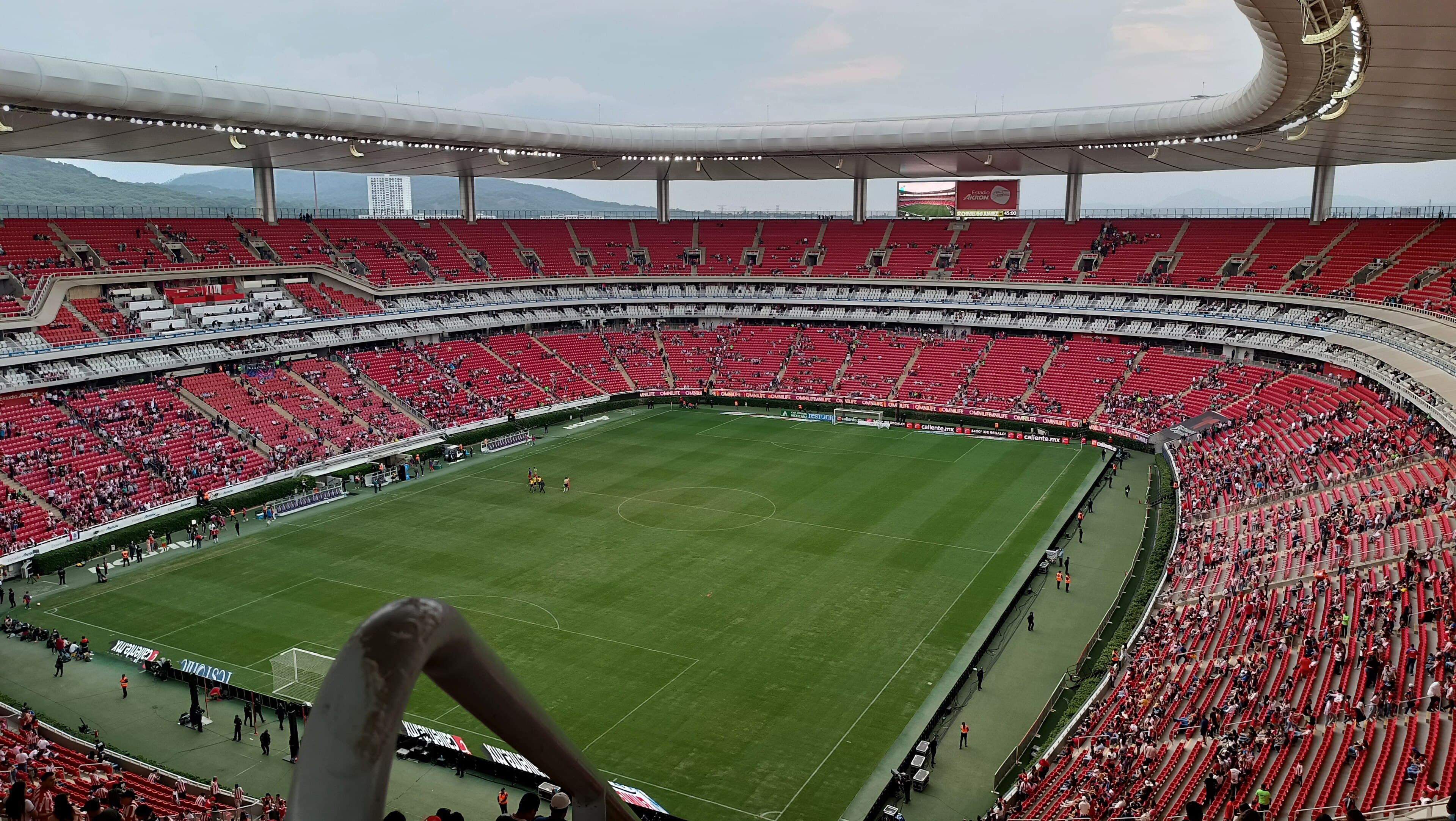 A large, modern football stadium with red seats and a green pitch, viewed from an elevated perspective under an open roof — illustrative photograph