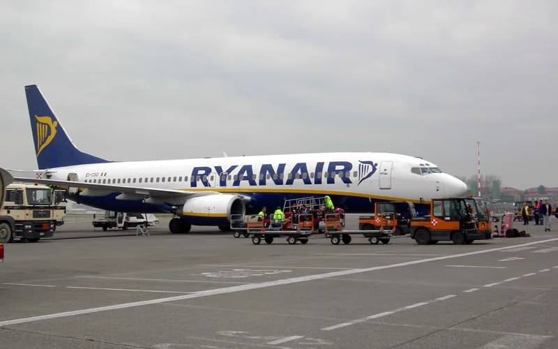 A ryanair aircraft is parked on the airport tarmac with ground crew and equipment nearby — illustrative photograph
