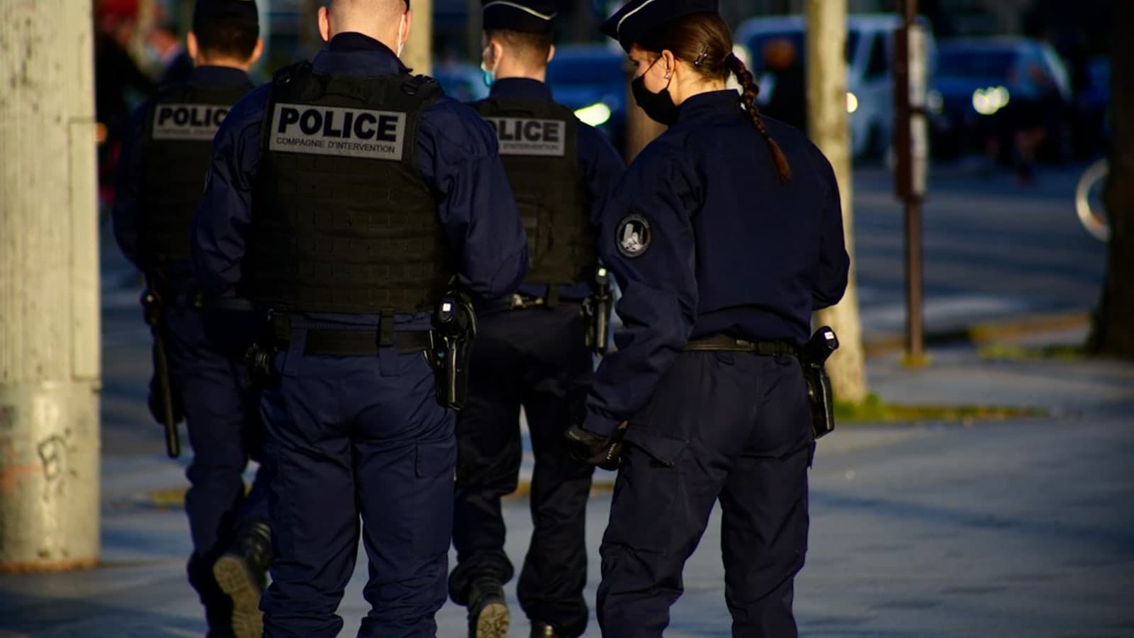 Four police officers in dark uniforms walk together on a city sidewalk at dusk — illustrative photograph