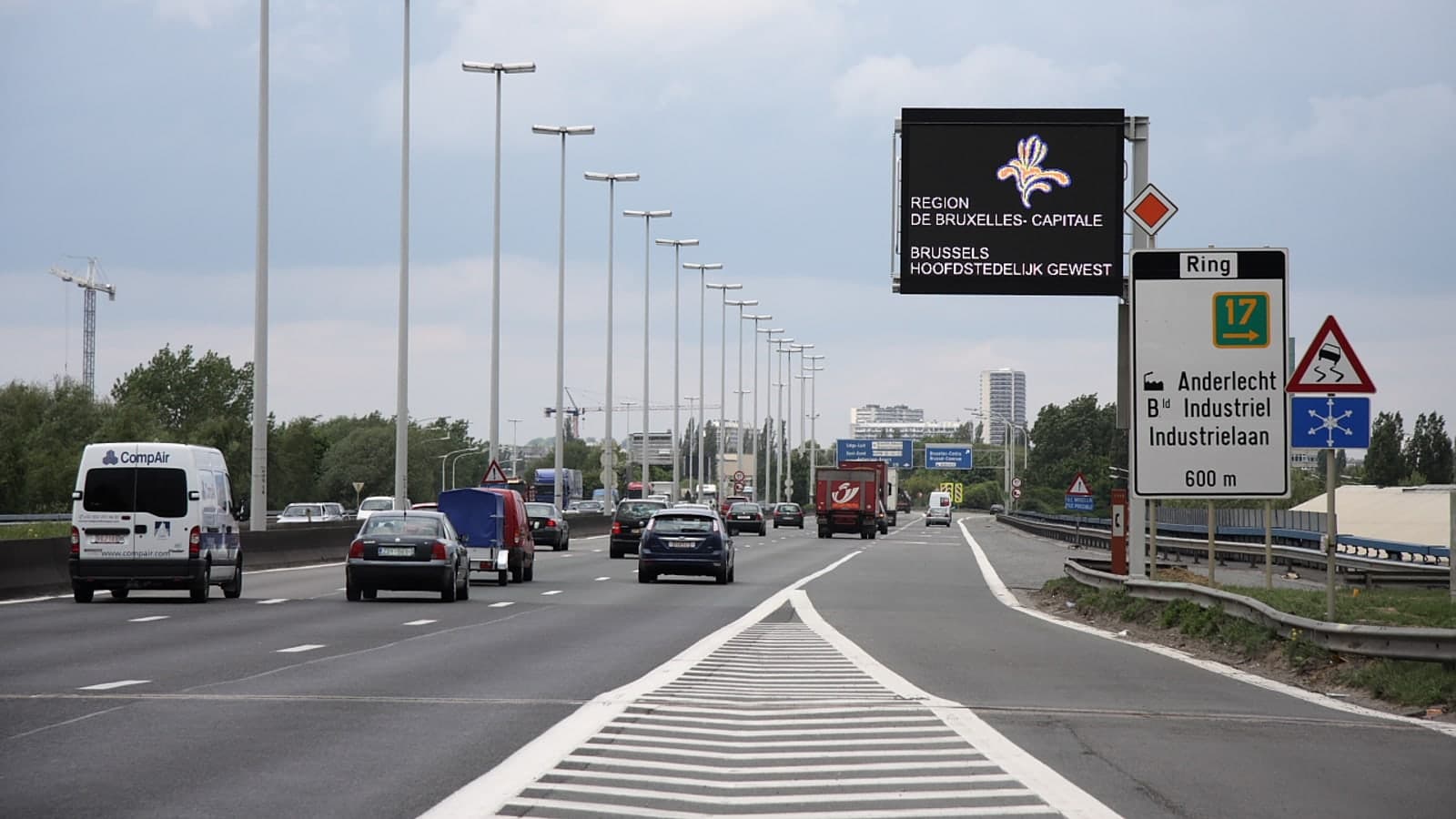 A multi-lane highway with vehicles traveling under clear skies, featuring prominent road signs indicating directions to brussels and… — illustrative photograph