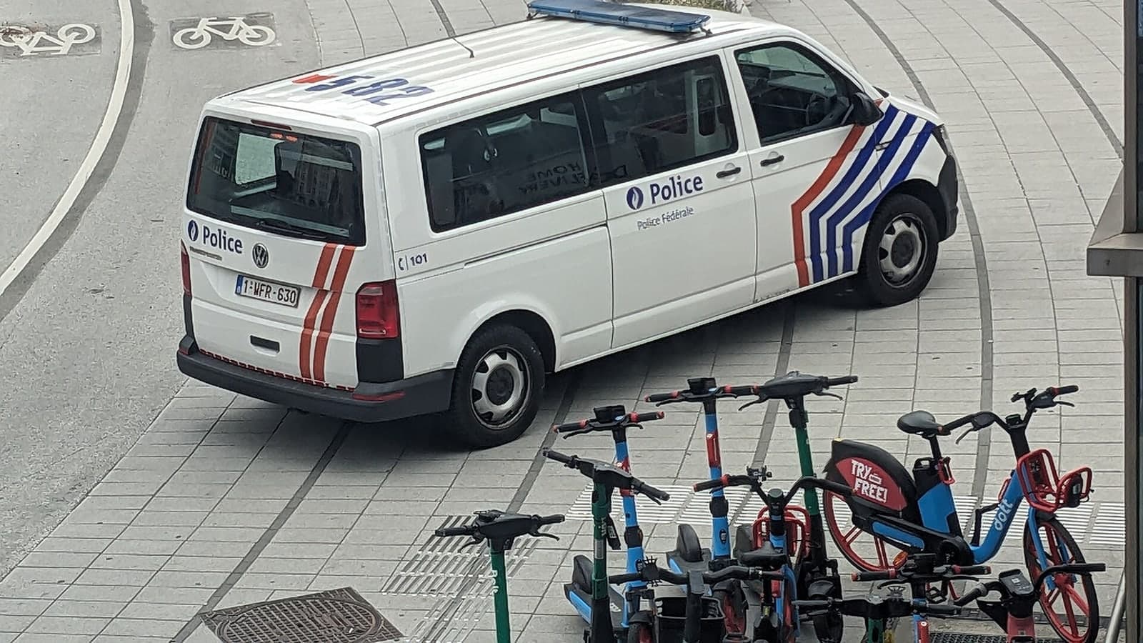 A white french police van is parked on a paved area near a row of shared electric scooters and bicycles — illustrative photograph