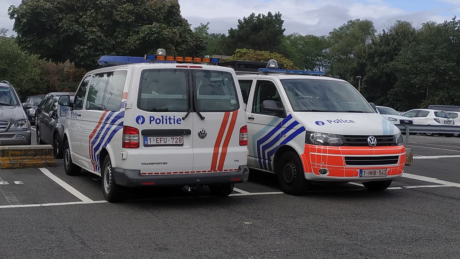 Two dutch police vans parked side by in a parking lot surrounded by trees and other vehicles — illustrative photograph