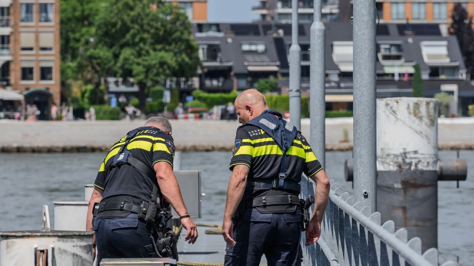 Two police officers patrol a riverside area, with buildings in the background — illustrative photograph