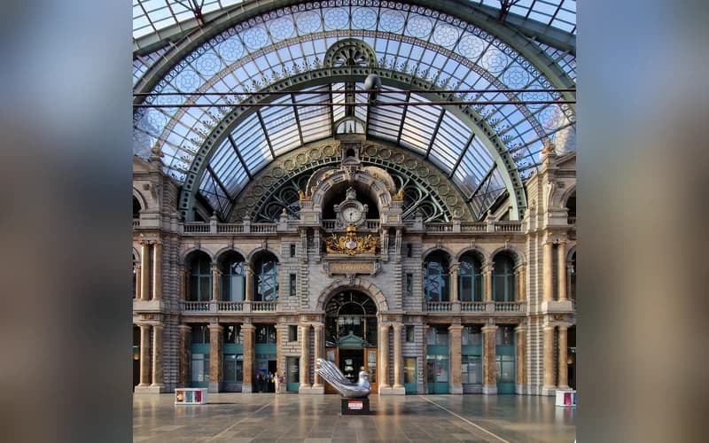 A grand, glass-domed train station interior with ornate architecture and a central clock — illustrative photograph